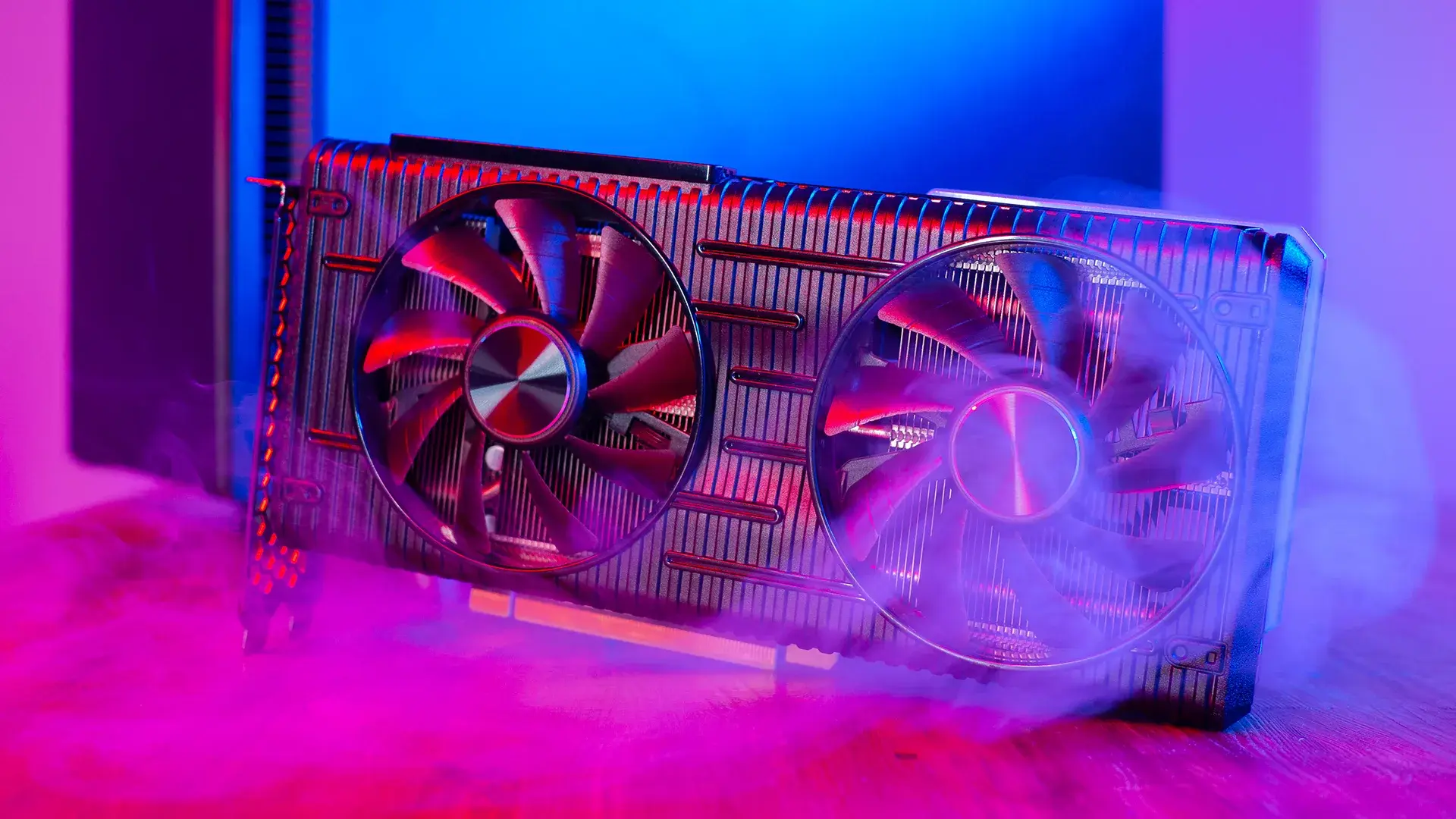 A dual-fan GPU graphics card lit by pink and blue neon lighting, with wisps of smoke drifting around it