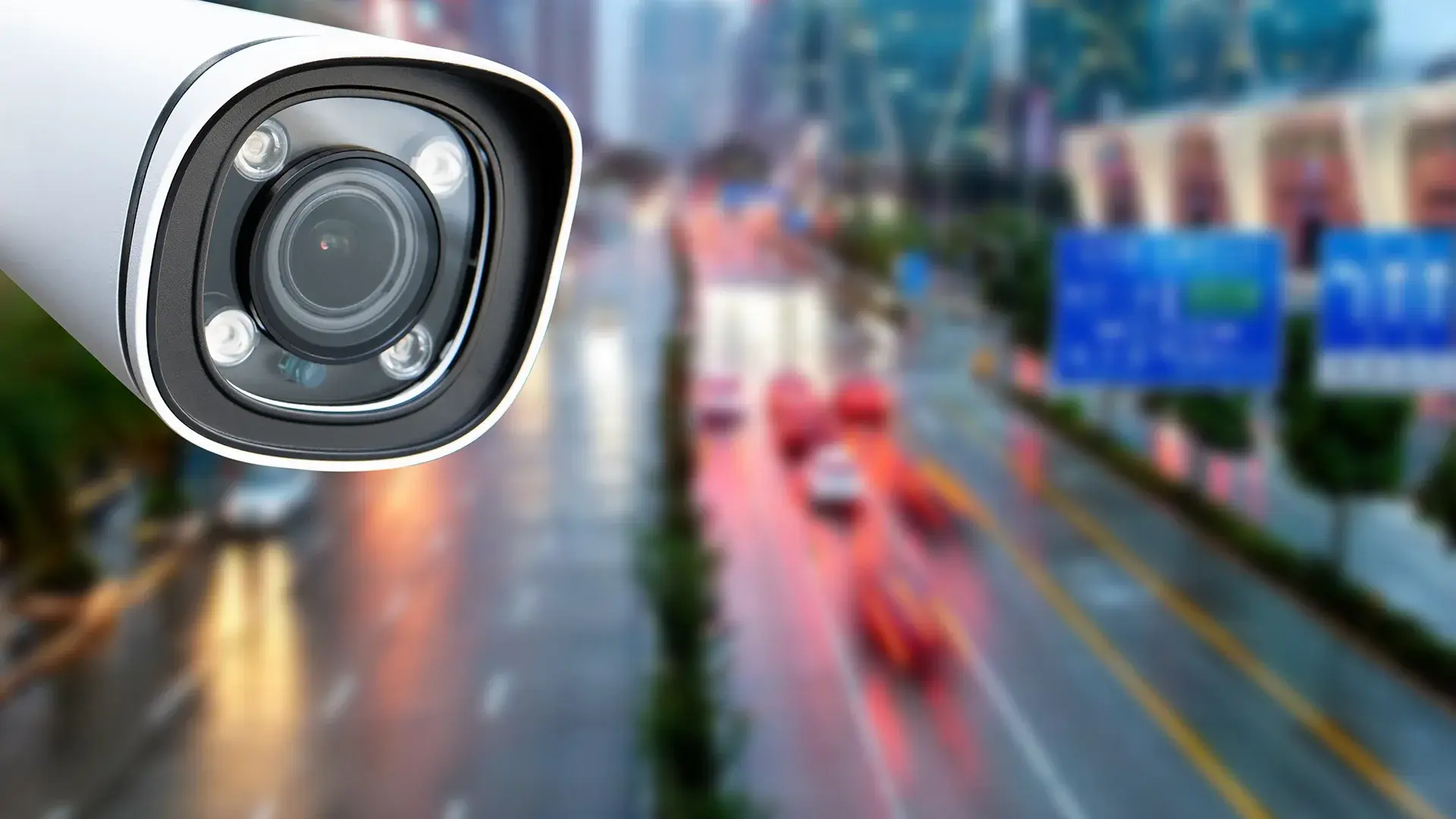 Camera-agnostic AI video analytics: a white bullet security camera monitoring a city street with blurred traffic in the background.