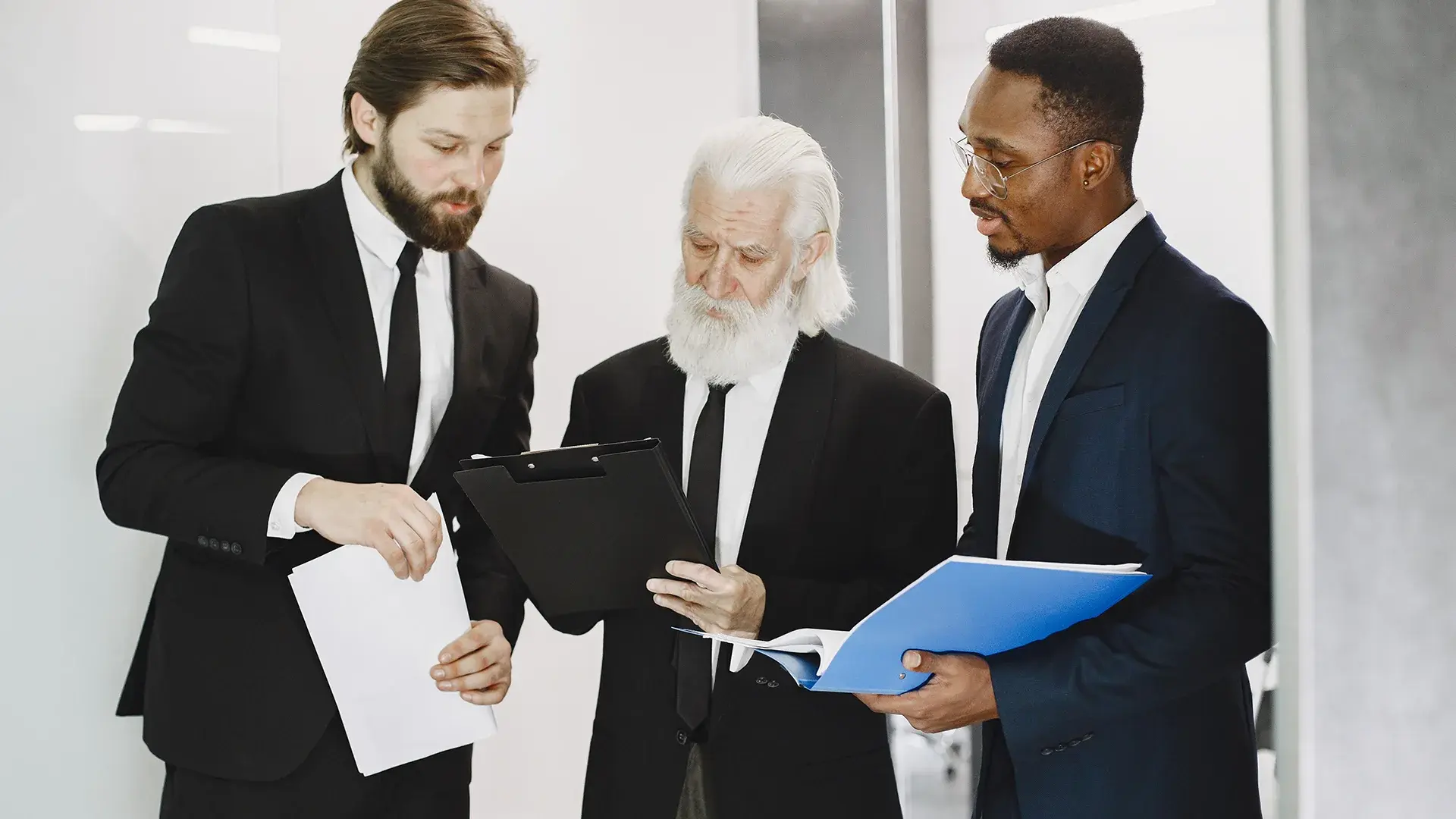 Three lawyers in suits reviewing case documents together in a law office
