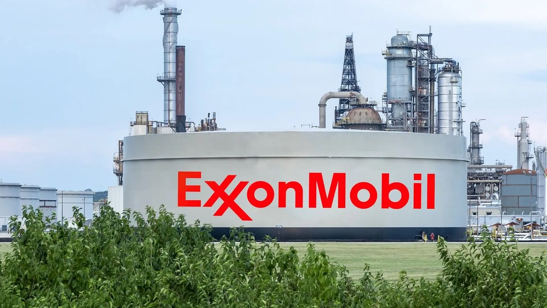 An ExxonMobil storage tank with industrial refinery structures in the background, representing the company’s operations in energy and petrochemical production