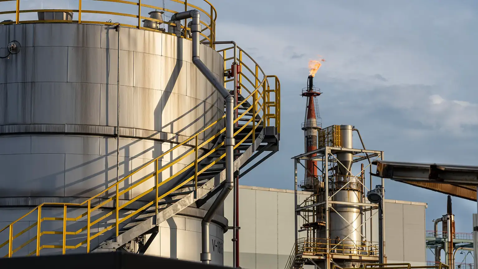 An ExxonMobil storage tank with industrial refinery structures in the background, representing the company’s operations in energy and petrochemical production
