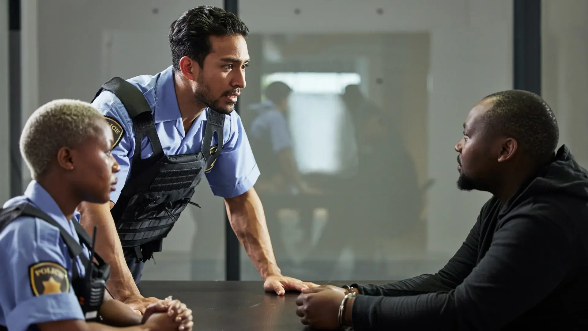 Police officers interviewing a handcuffed suspect in an interrogation room.
