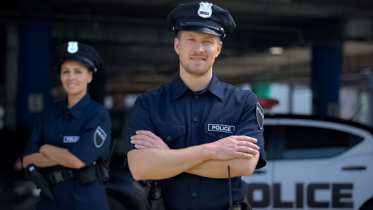 Two police officers in uniform, standing confidently with arms crossed in front of a police vehicle, ready for duty.