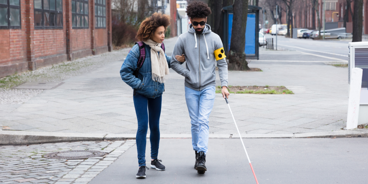 A video of a woman helping a blind man cross the street. 