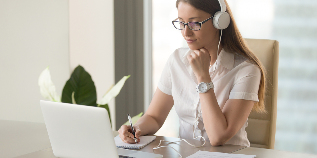 A woman writing on a notepad in front of her laptop